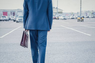 Açık otoparkta mavi takım elbiseli ve kahverengi çantalı bir işadamı. .