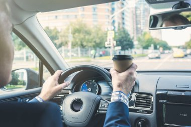 Yaşlı iş adamı otoyolda araba sürerken kağıt bardaktan kahve içiyor. Seçici odak