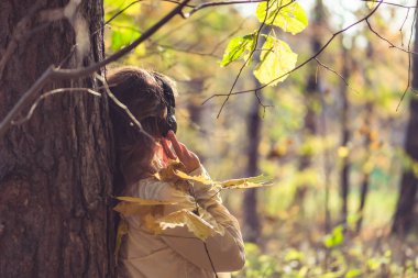 Kulaklıklı bir kadın parkta büyük bir akçaağacın yanında duruyor ve sonbahar ormanında müzik dinliyor. Kavram. Hint yaz sezonu