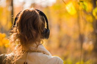 Kulaklıklı bir kadın parkta büyük bir akçaağacın yanında duruyor ve sonbahar ormanında müzik dinliyor. Kavram. Hint yaz sezonu