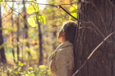 Kulaklıklı bir kadın parkta büyük bir akçaağacın yanında duruyor ve sonbahar ormanında müzik dinliyor. Kavram. Hint yaz sezonu