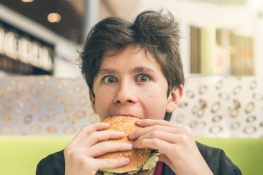 Kafede hamburger yiyen genç bir çocuk. 