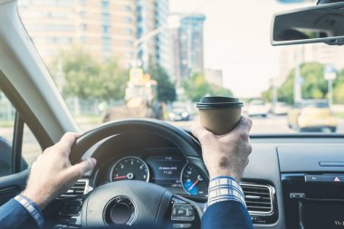 Yaşlı iş adamı otoyolda araba sürerken kağıt bardaktan kahve içiyor. Seçici odak