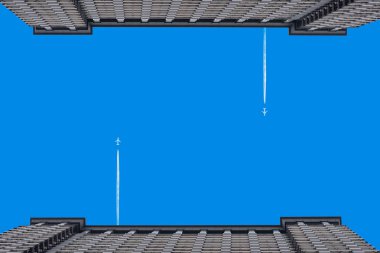 Köprünün üstünde, iki bina arasında açık mavi gökyüzünde bir uçak.