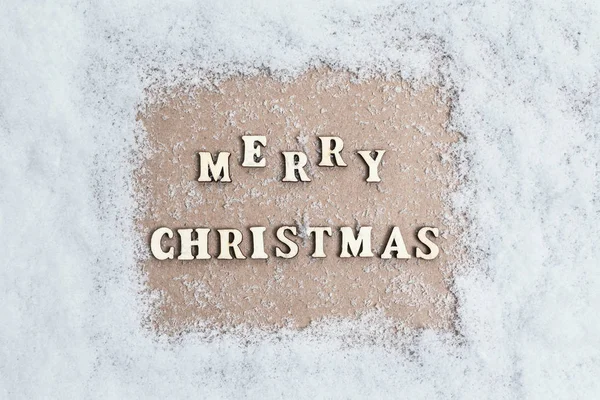 View from above. snow texture. craft paper in the middle with with the inscription merry christmas from wooden letters. Concept