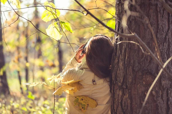 Kulaklıklı bir kadın parkta büyük bir akçaağacın yanında duruyor ve sonbahar ormanında müzik dinliyor. Kavram. Hint yaz sezonu