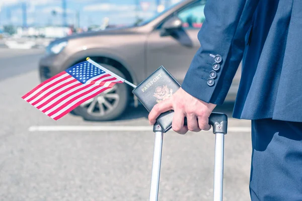 Man pilot in a blue uniform (suit), suitcase flag and american passport. airport parking rental car. concept