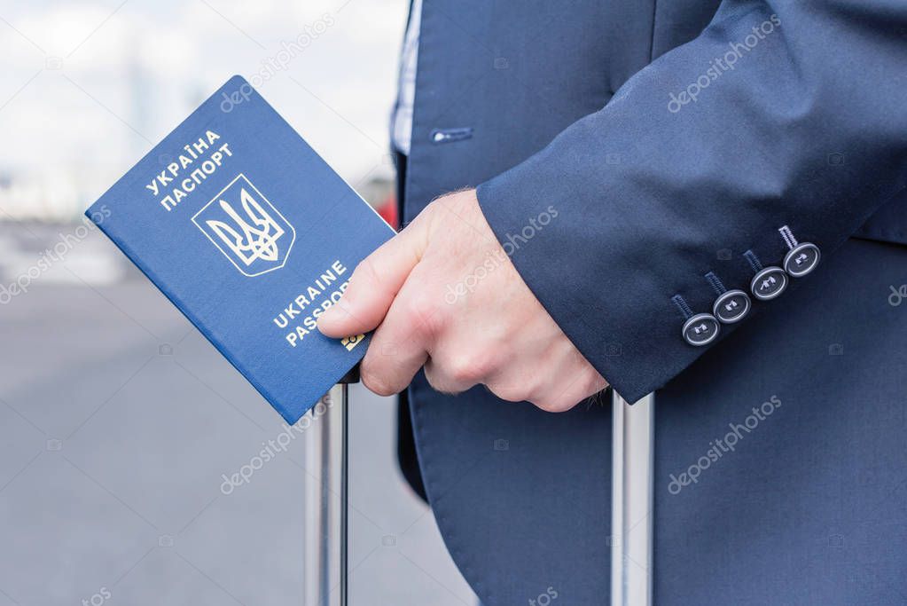 man in a blue suit with a suitcase and a ukrainian passport at the airport. Business trip concept