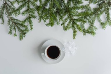 Bir fincan sade kahve ve beyaz bir masanın üzerinde ladin dallarında parlayan kar tanesi. Noel ve Yeni Yıl konsepti. Kahve sanatı. Düz yatış, üst görünüm. 