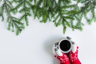 Beyaz bir masanın üzerinde ladin dallarında bir fincan sade kahve ile kış eldivenleri giymiş kadın eller. Noel ve Yeni Yıl konsepti. Kahve sanatı. Düz yatış, üst görünüm. 