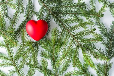 Beyaz bir masada ladin dallarında büyük kırmızı bir kalp. Noel ve Yeni Yıl konsepti. Düz yatış, üst görünüm. 