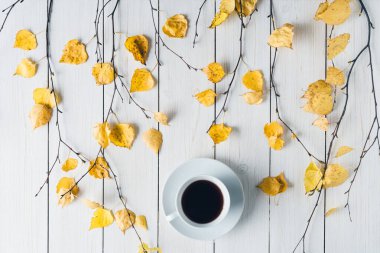 Ağaç dallarında bir fincan kahve ve beyaz tahta üzerinde sarı yapraklar olan bir kadın. Geçmişi. Sonbahar, sonbahar konsepti. Düz yerde, üst tarafta. Kahve sanatı