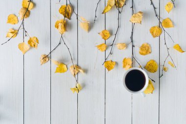 Ağaç dallarında bir fincan kahve ve beyaz tahta üzerinde sarı yapraklar olan bir kadın. Geçmişi. Sonbahar, sonbahar konsepti. Düz yerde, üst tarafta. Kahve sanatı