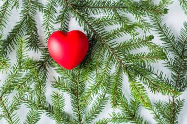 Beyaz bir masada ladin dallarında büyük kırmızı bir kalp. Noel ve Yeni Yıl konsepti. Düz yatış, üst görünüm. 