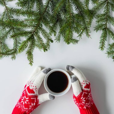 Beyaz bir masanın üzerinde ladin dallarında bir fincan sade kahve ile kış eldivenleri giymiş kadın eller. Noel ve Yeni Yıl konsepti. Instagram. Düz yatış, üst görünüm. 
