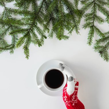 Beyaz bir masanın üzerinde ladin dallarında bir fincan sade kahve ile kış eldivenleri giymiş kadın eller. Noel ve Yeni Yıl konsepti. Kahve sanatı. Düz yerde, üst tarafta. Instagram