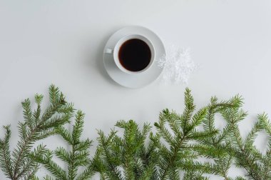 Bir fincan sade kahve ve beyaz bir masanın üzerinde ladin dallarında parlayan kar tanesi. Noel ve Yeni Yıl konsepti. Kahve sanatı. Düz yatış, üst görünüm. 