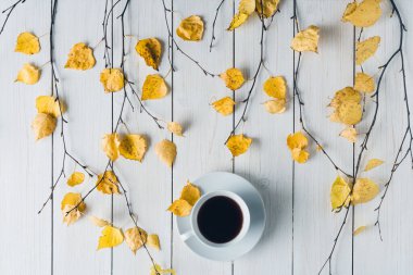 Ağaç dallarında bir fincan kahve ve beyaz tahta üzerinde sarı yapraklar olan bir kadın. Geçmişi. Sonbahar, sonbahar konsepti. Düz yerde, üst tarafta. Kahve sanatı