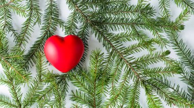 Beyaz bir masada ladin dallarında büyük kırmızı bir kalp. Noel ve Yeni Yıl konsepti. Düz yatış, üst görünüm. 