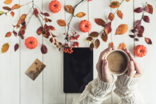 Woman with tablet and credit (discount) card cup on white retro wood boards. Coffee, tablet, leaves, rowan and small pumpkins . Autumn, fall concept. Flat lay, top view.