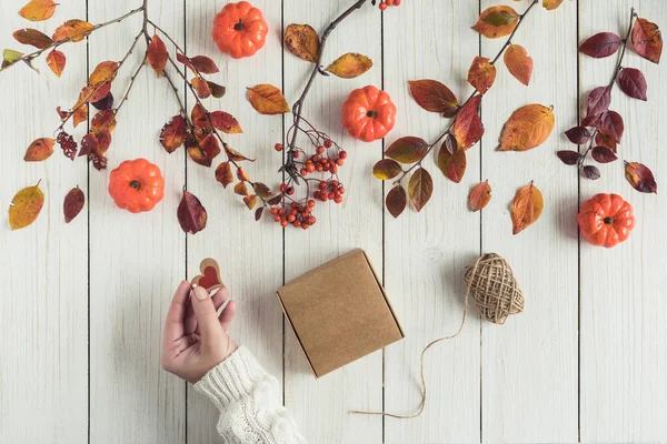 Woman packing gift in a box of kraft paper on white retro wood boards. leaves, rowan and small pumpkins. Thanksgiving. Autumn, fall concept. Flat lay, top view.
