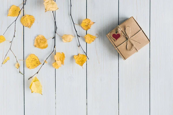 Woman packing gift in a box of kraft paper on white retro wood boards. leaves, birch branches. Thanksgiving. Autumn, fall concept. Flat lay, top view.