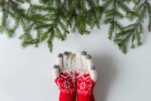 Female hands in the winter gloves with glowing snowflake in spruce branches on a white table. Christmas and New Year concept.  Flat lay, top view.