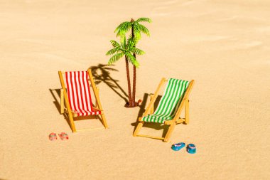 İki güverte sandalyesi, güneş yatağı, dinlenme odası, parmak arası terlik, kumsaldaki palmiye ağacı. Yaz ve seyahat konsepti. Minimalizm