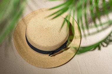 Palmiye dalları ve gölgeli palmiye ağaçları arasında kum üzerinde yaz hasarı şapkası. Seyahat, tatil, yaz tatili konsepti. Üst görünüm.
