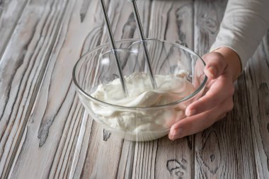 Gri kırsal ahşap masada elektrikli el mikseri kullanan krem şanti kullanan bir kadın. 