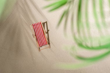 Hava manzaralı iki iskemle, bir bardak meyve suyu, palmiye dalları ve gölge palmiye dalları arasında kum üzerinde parmak arası terlikler. Seyahat, tatil, yaz tatili, romantik konsept. Üst görünüm.