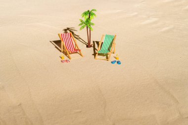 İki güverte sandalyesi, güneş yatağı, dinlenme odası, bir bardak portakal suyu, parmak arası terlik, kumsalda palmiye ağacı. Yaz ve seyahat konsepti. Minimalizm