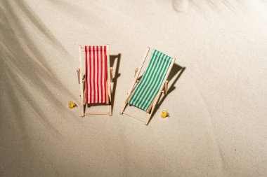 Hava manzaralı iki iskemle, bir bardak meyve suyu, palmiye dalları ve gölge palmiye dalları arasında kum üzerinde parmak arası terlikler. Seyahat, tatil, yaz tatili, romantik konsept. Üst görünüm.