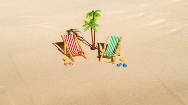 İki güverte sandalyesi, güneş yatağı, dinlenme odası, bir bardak portakal suyu, parmak arası terlik, kumsalda palmiye ağacı. Yaz ve seyahat konsepti. Minimalizm
