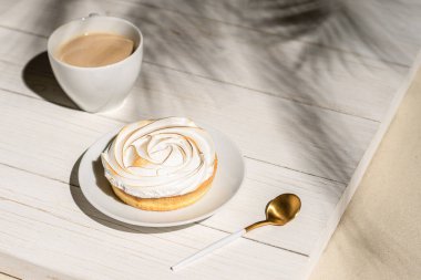 Tahtaya konmuş limonlu küçük turta palmiye dallarının gölgelerindeki açık hava kafeteryasında masa. Bir fincan kahveyle Avrupai kahvaltı.