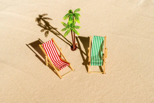 Aerial view of two deck chair, sunbed, lounge, palm tree on sandy beach. Summer and travel concept. Minimalism