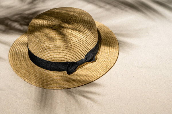 Summer straw hat on sand through the branches of palm and shadow palm tree. Travel, holiday, summertime concept. Top view.