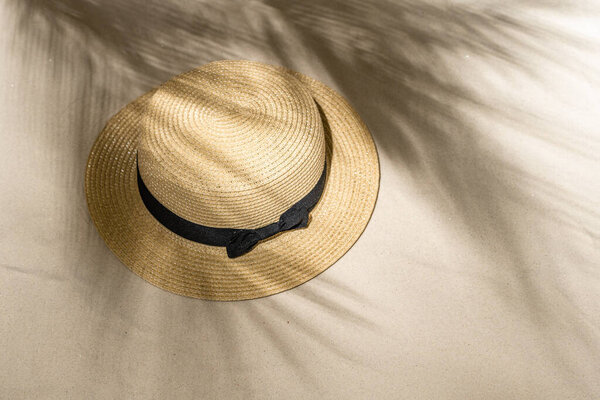 Summer straw hat on sand through the branches of palm and shadow palm tree. Travel, holiday, summertime concept. Top view.