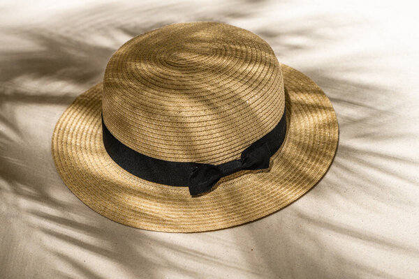 Summer straw hat on sand through the branches of palm and shadow palm tree. Travel, holiday, summertime concept. Top view.