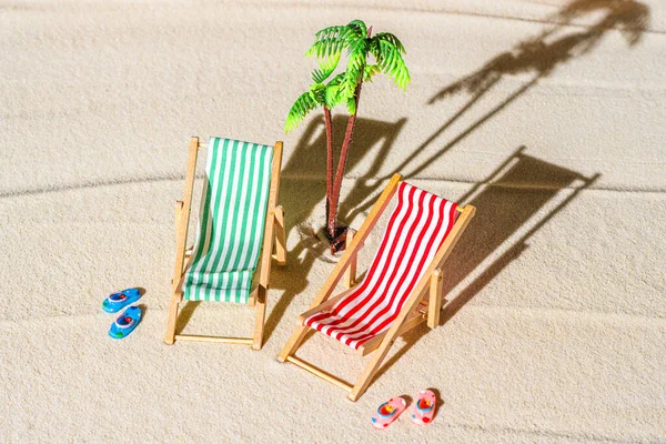 Aerial view of two deck chair, sunbed, lounge, flip flops, palm tree on sandy beach. Summer and travel concept. Minimalism