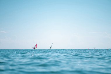 Gün batımında denizdeki rüzgar sörfçüleri ufukta. Deniz dalgasını kapat, alçak açılı görüş. Seçici odaklanma, bokeh