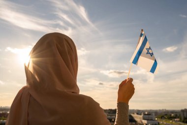 Mavi günbatımı göğünde İsrail bayrağı taşıyan başörtüsü takmış Müslüman kadın silueti. Özgürlük kavramı
