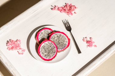 Ejderha meyvesi, pitaya, tropik plajın kumsalında, bir palmiye ağacının altında beyaz bir ahşap tepside. Egzotik yemekler, atıştırmalıklar. Yaz seyahati