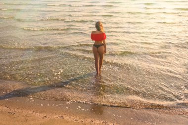 Bikinili, kısa bluzlu, kumlu bir sahilde yürüyen ve dinlenen güzel bir kız. Üst görünüm.