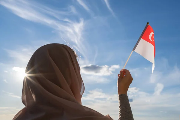 青い夕日の空にシンガポールの旗を頭スカーフでイスラム教徒の女性のシルエット 自由の概念 — ストック写真