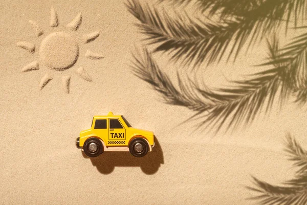 Toy taxi car, sun, palm tree on beach sand. Concept. Fast and cheap taxi booking service. Travel. Summer time. Creative