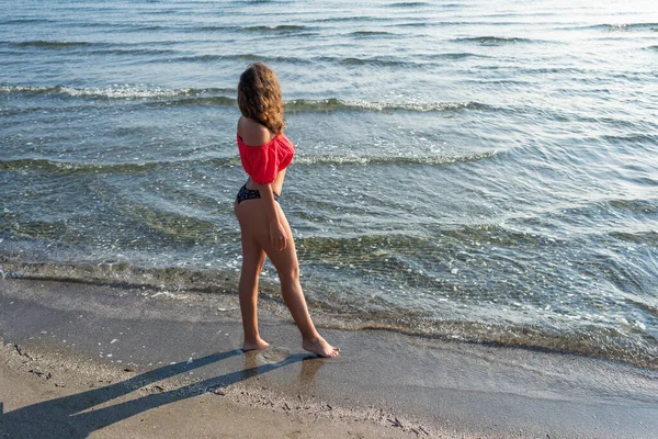 Beautiful girl in a bikini and a short blouse walking and relaxing on a sandy beach by the sea wave. Top view.