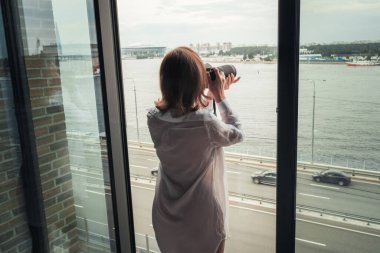 Açık panoramik apartman penceresinin yanında kamerayla fotoğraf çeken şeffaf gecelikli kadın fotoğrafçının arka planı.. 