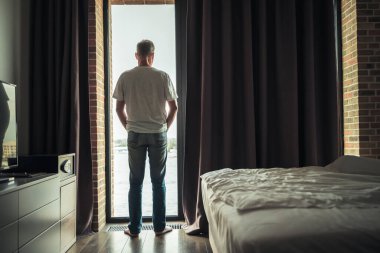 Issız, orta yaşlı, kır saçlı bir adamın, açık pencere ya da otel odasının yakınında dikilirken,.