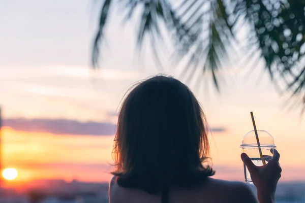 后视镜上是一个漂亮的女孩 她把矿泉水放在玻璃杯里 背对着海的棕榈树枝头 日落海滩 夏天和自由的概念 — 图库照片